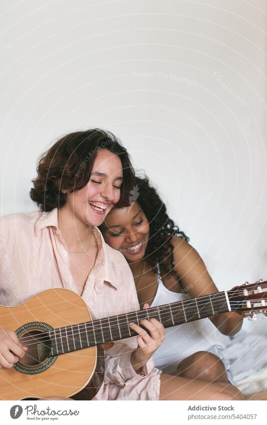 Cheerful lesbian couple playing guitar at home girlfriend cheerful leisure enjoy together music fun bed women happy chill multiracial relationship multiethnic