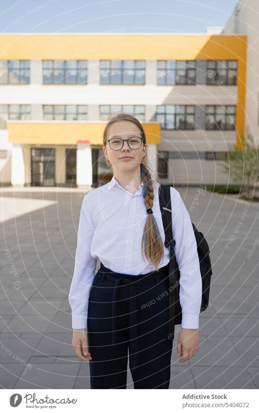 Positive teenage schoolgirl standing with bag near building uniform student back to school adolescent pupil backpack education serious glass friendly positive