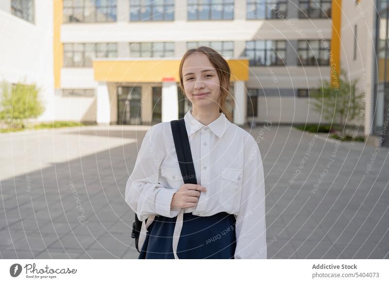 Happy teenage schoolgirl standing with bag near building smile uniform student back to school adolescent pupil backpack education glass friendly happy glad