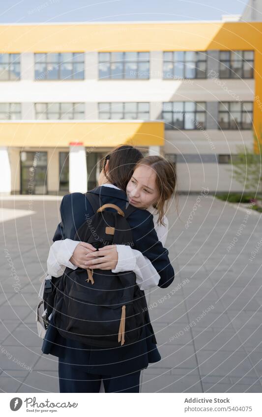 Happy schoolgirls standing and embracing near school building student teenage campus hug smile classmate embrace adolescent young friend pupil backpack uniform