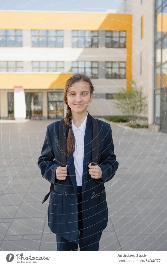 Confident young teenage schoolgirl standing with backpack uniform student adolescent smile pupil building cheerful happy education friendly study positive glad