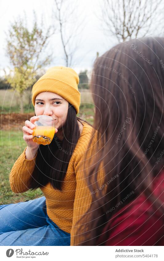 Ladies drinking orange juice during picnic in park in autumn park women friend glass countryside smile plaid female enjoy lawn blanket beverage spend time grass