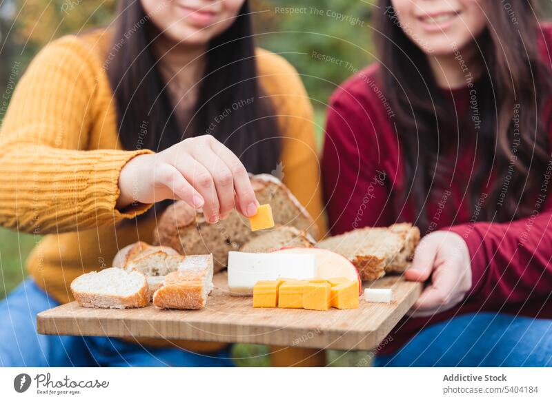 Anonymous female friends eating together in countryside women picnic bread food cheese chopping board park cutting board enjoy lawn spend time grass free time