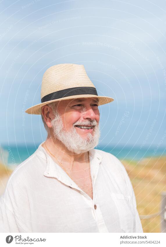 Cheerful senior man in hat standing on beach happy portrait retire smile elderly glad coast holiday cheerful seashore ocean vacation summer positive coastline