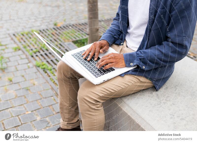 Anonymous crop black man using laptop on street freelance computer remote work project browsing internet male african american entrepreneur self employed