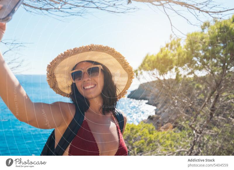 Young woman taking selfie with ocean tourist smartphone self portrait sea tropical resort hat female balearic islands take photo picture memory mobile tourism