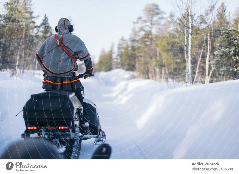 Anonymous person in gakti riding snowmobile in winter forest saami ride authentic indigenous drive transport road countryside nordic native season cold frost