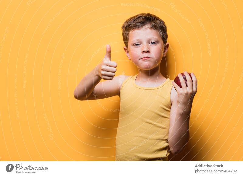 Cute boy showing thumbs up while holding apple thumb up gesture child approve sign ripe fruit portrait kid schoolboy positive vivid casual recommend cute