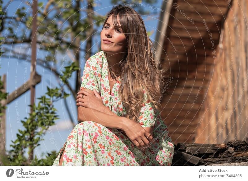 Calm female in sundress near country house woman countryside summer leisure rest daydream porch romantic idyllic season relax calm weekend long hair tranquil