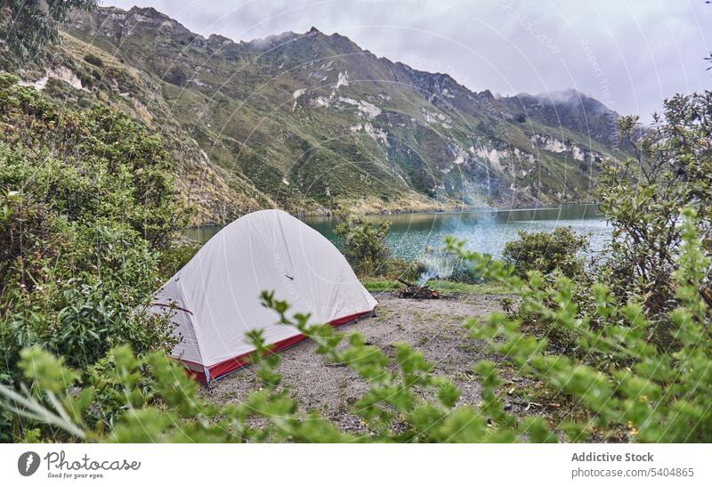 Camping tent on rocky shore of lake in daylight mountain hill nature camp highland landscape cloudy adventure scenery campsite valley tree sky picturesque green