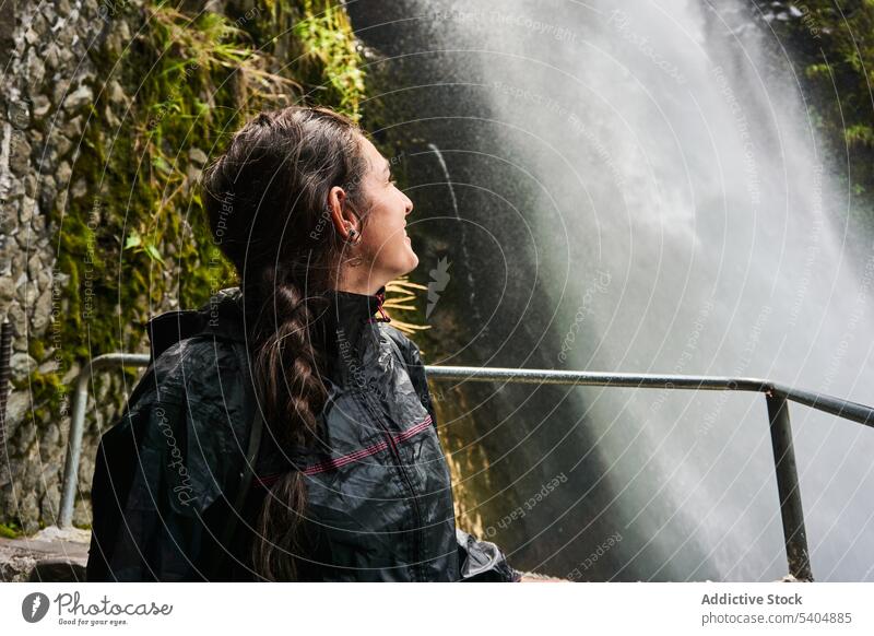 Young woman traveler standing and looking at waterfall tourist watch explore backpack smile vacation railing enjoy adventure journey young female tourism