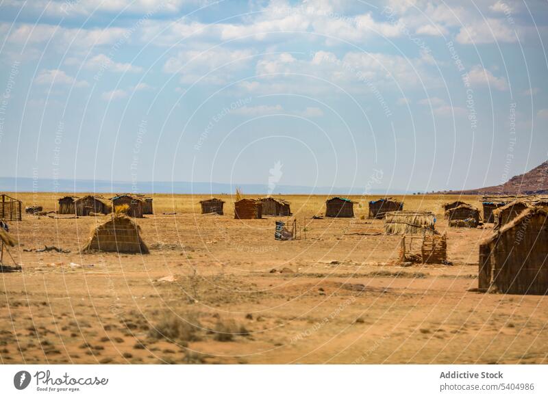Group of barn huts on dry terrain in bright sunlight hay settlement arid rural blue sky countryside landscape cloudy desert environment grass madagascar africa