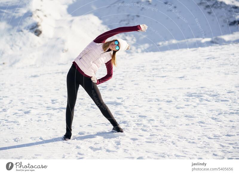 Slim woman in sportswear stretching arm sideway in snowy mountains winter yoga exercise practice healthy training activity slope young female nature wellness