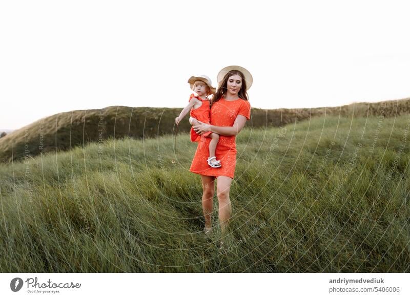 young beautiful mother and little daughter walking on nature on summer day vacation. Mom and girl playing in the field at the sunset time. mothers day. Concept of friendly family