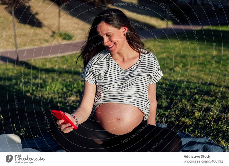 Pregnant woman with smartphone in park pregnant expect belly lotus pose mobile blanket mat female await childbearing maternal prenatal anticipate mindfulness