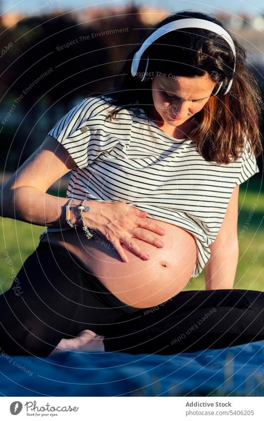 Happy expecting woman on grass await belly headphones listen music blanket mat female pregnant childbearing maternal prenatal anticipate mother parent mom