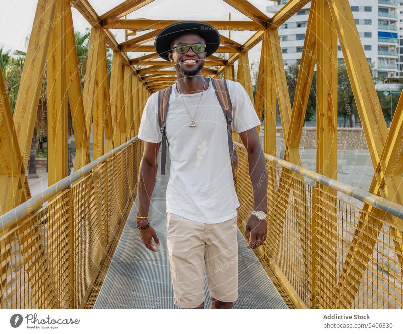 Smiling black guy walking on footbridge in park man trendy smile tourist positive style city happy male young african american ethnic fashion hat cheerful