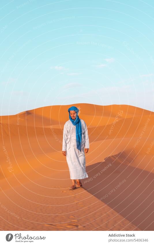 Smiling Berber man in traditional clothes walking in desert berber tuareg sand dune nature travel male moroccan morocco young sky summer landscape blue africa