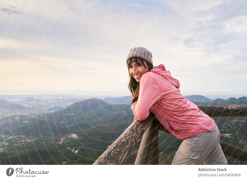 Glad woman leaning on fence in mountains tourist traveler railing admire highland observe vacation viewpoint female trip smile tourism lady cheerful wanderlust