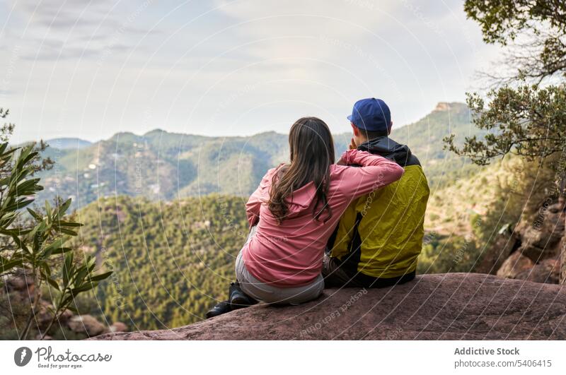 Unrecognizable couple sitting on mountain tourist viewpoint admire highland observe embrace edge affection vacation traveler trip tourism idyllic freedom