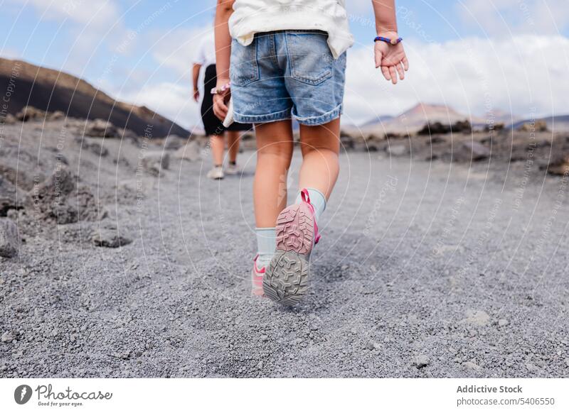 Unrecognizable male and kid walking on dry terrain in daylight man child follow sneakers arid countryside landscape summer together blue sky sun childhood