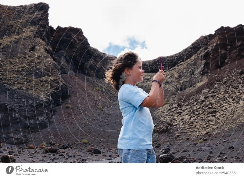 Smiling child taking photos on smartphone in mountainous terrain kid traveler using take photo volcano explore crater landscape adventure girl rock gadget