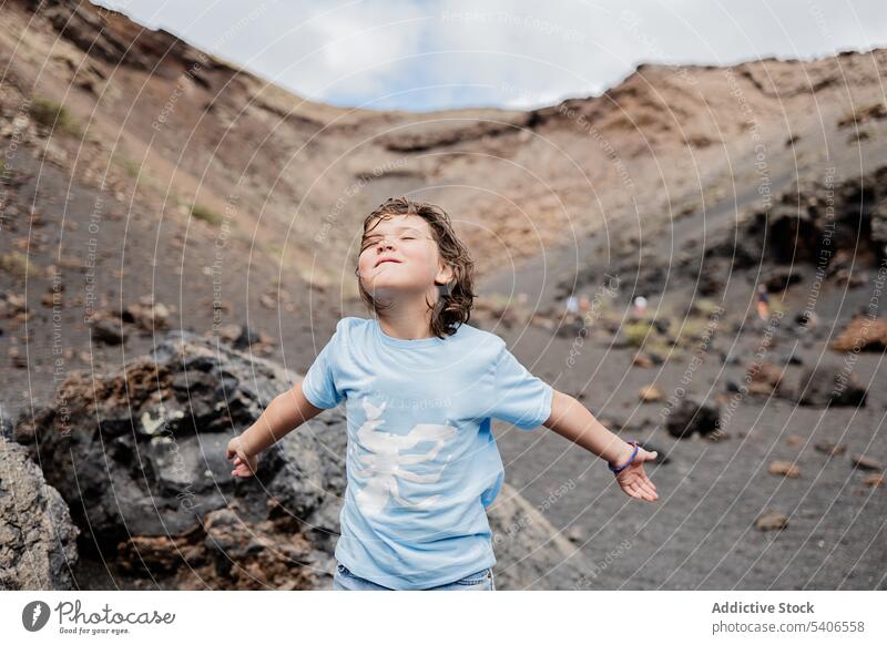 Happy kid standing on rocky formation in mountainous area child smile stone boulder enjoy blue sky content summer girl happy highland childhood preteen admire