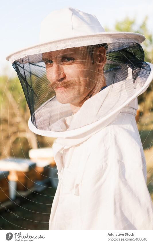 Male beekeeper working in apiary in sunny day man field workwear uniform protect summer mask costume male adult mature senior white worker safety serious green