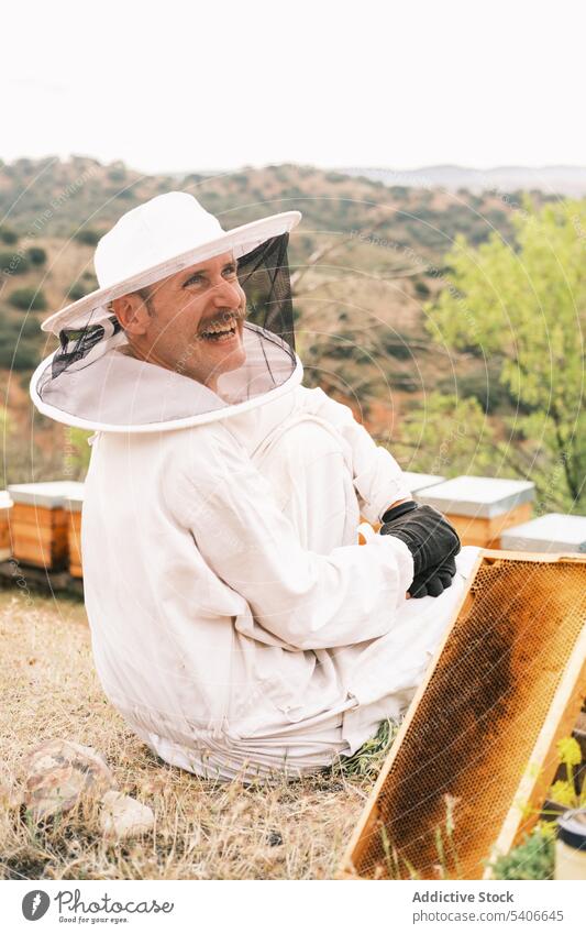Happy beekeeper with part of beehive in apiary cheerful protect costume smile honeycomb man male uniform job nature professional happy farmer countryside work