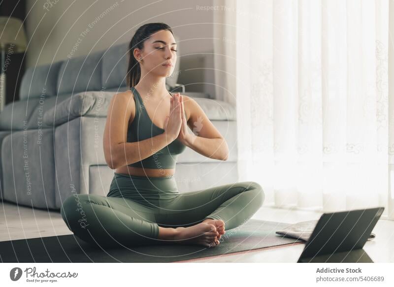 Beautiful young woman doing online yoga at home sportswoman lotus pose meditate padmasana mindfulness calm relax practice mat female slim wellness zen position