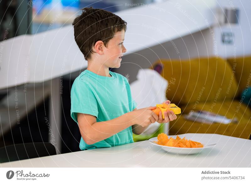 Little boy standing at table with fresh carrot in kitchen kid slice plate help sharpener busy child home childhood vitamin nutrition casual prepare natural