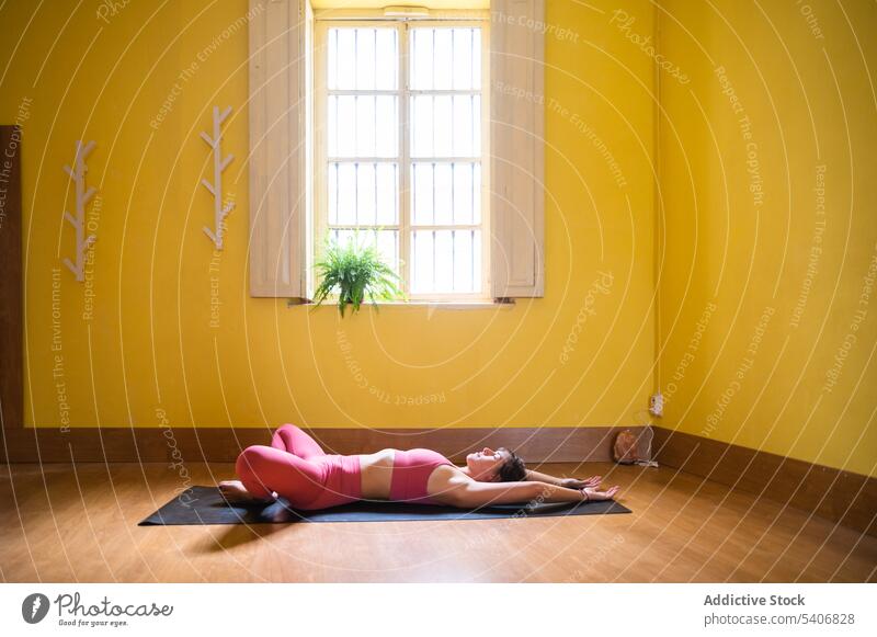 Flexible woman lying on mat and practicing Supine Bound Angle yoga in pose practice supta baddha konasana eyes closed flexible room young female mindfulness