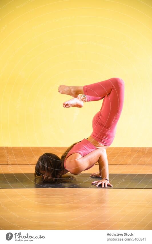 Unrecognizable slim woman on mat doing Scorpion yoga in pose in daylight balance flexible vrischikasana practice inversion wall young female sportswear calm