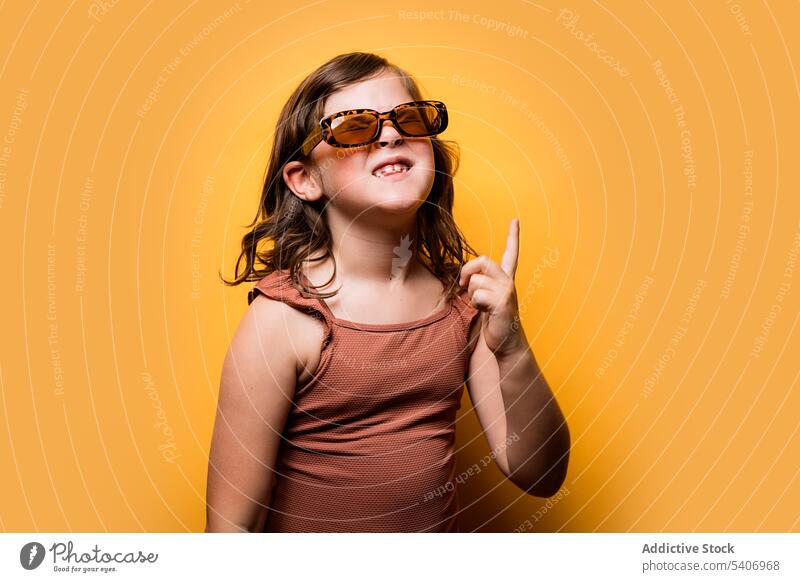Delighted little kid in summer outfit pointing up in orange studio girl point up eyes closed happy cheerful funny having fun gesture portrait child index finger