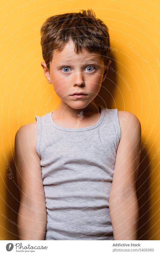 Shocked kid looking at camera with astonishment in yellow studio boy shock gaze surprise expressive wow scare portrait child amazed unexpected brown hair top