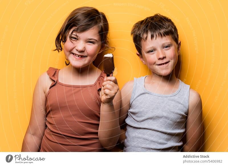 Happy girl holding ice cream while standing with boy in studio children chocolate bar treat sweet summer funny grimace cheeky expressive cheerful smile happy