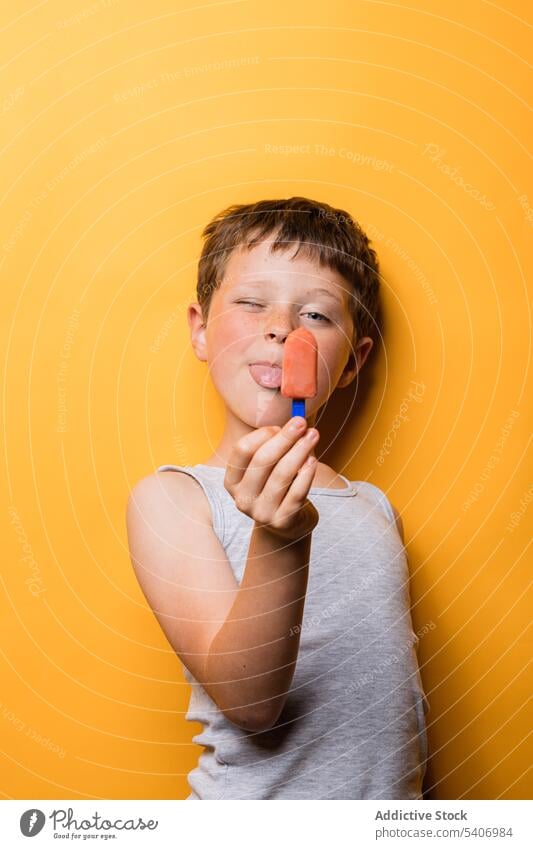 Funny boy showing tongue while eating ice pop kid show tongue tongue out lick ice cream grimace make face studio shot cheerful funny child fruit cold cool chill