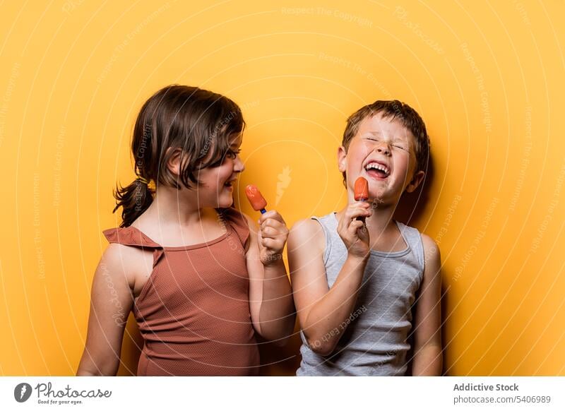 Cheerful boy and girl eating ice pops in studio children having fun laugh popsicle childhood ice cream funny expressive humor joke carefree smile happy cheerful