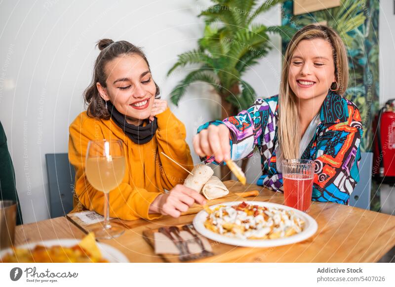 Cheerful friends having fun with drinks and plates of food at table women eat smile positive snack beverage meal dinning table casual cheerful friendship