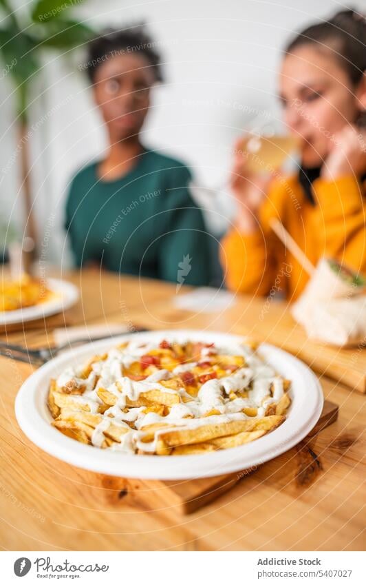 Delicious cheese loaded fries on table with blurred people on background creamy delicious dish plate food yummy eat lunch friend fried tasty wooden serve meal