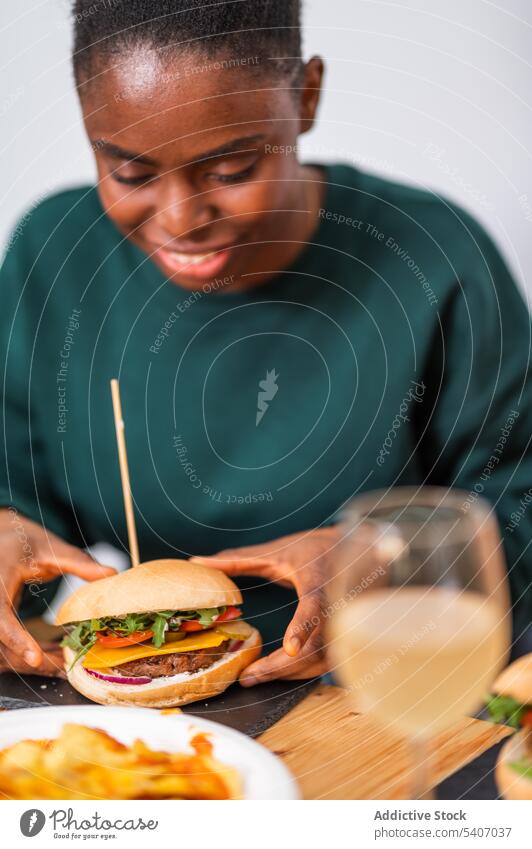 Smiling African American woman eating delicious burger tasty snack restaurant cafeteria portion food young hungry dish plate yummy table meal hamburger lunch