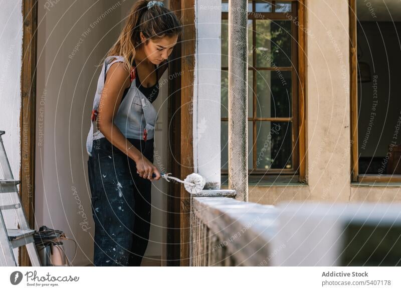 Focused woman painting on balcony with roller painter renovate fence house tool improve wooden casual daytime home female apartment young construction