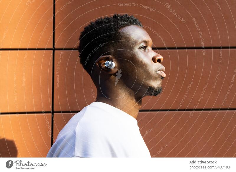 Serious young black man standing near wall listen portrait music serious earphones t shirt pensive male true wireless tws african american earbuds device song