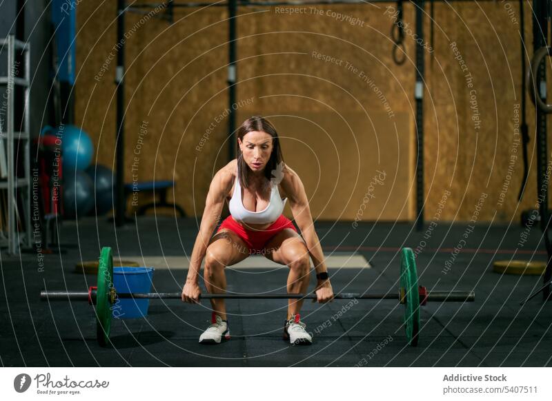 Strong focused sportswoman lifting barbell in gym squat weightlifting overhead exercise heavy mature training fitness healthy equipment serious intense sporty