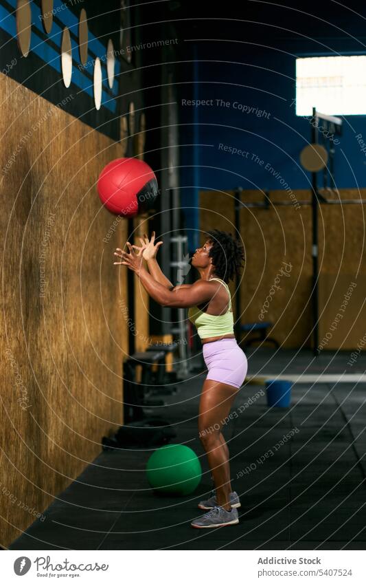Strong black sportswoman throwing medicine ball against wall exercise power weight training gym mature african american ethnic afro equipment muscular intense