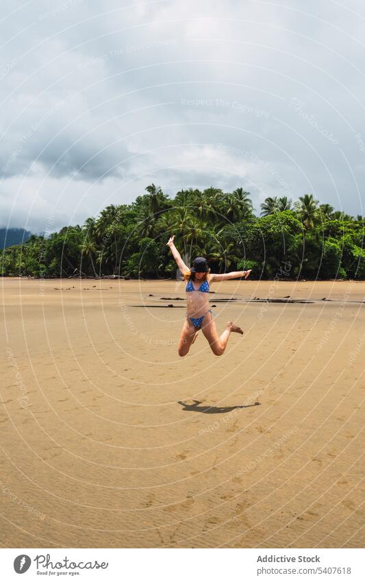 Carefree woman jumping on sandy beach resort sunlight freedom arms raised carefree shore having fun joy excited energy female young uvita puntarenas costa rica