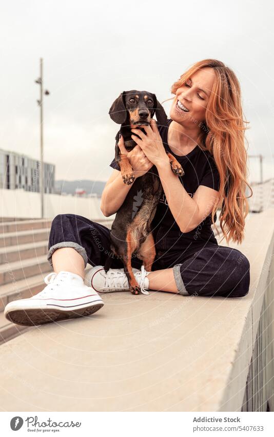 Happy woman embracing dog on street owner hug dachshund stroke caress love pet smile joy happy female young redhead casual long hair embrace animal together