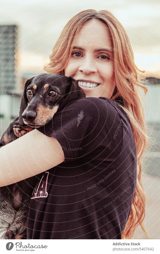 Happy female owner embracing dog on street woman hug care close dachshund love pet smile happy toothy smile young redhead casual long hair city canine loyal