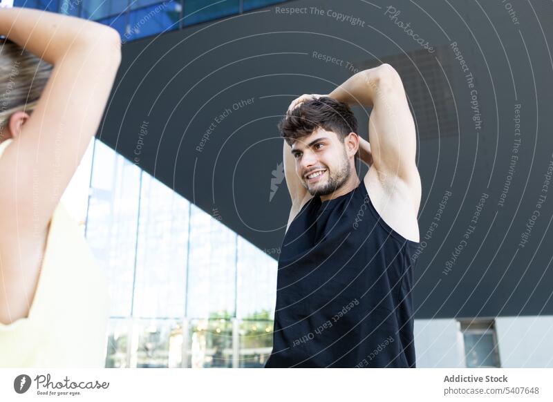 Young man with raised arms doing warmup with unrecognizable woman exercise warm up workout practice smile positive glad arms folded male female young wellness