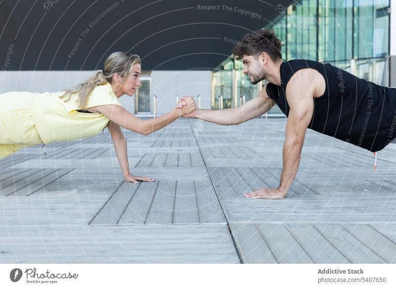 Confident couple doing plank exercise with holding hands in open place training stretch relationship happy workout floor young fitness love romantic affection